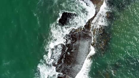 Beautiful-bird's-eye-top-aerial-drone-spinning-shot-of-waves-crushing-into-a-black-rock-in-the-beach-at-Sibauma-creating-a-natural-swimming-pool-during-low-tide-near-Pipa-in-Northern-Brazil