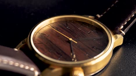 Close-up-of-luxury-golden-watch-with-wooden-dial-and-black-background