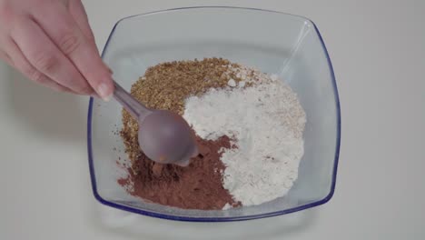 Adding-tablespoon-of-cocoa-powder-to-dry-ingredients-in-mixing-bowl,-Overhead