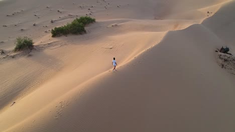 Guy-walking-alone-on-a-huge-sand-dune-in-the-middle-of-the-desert-while-the-drone-spins-around-the-individual-revealing-the-scenery