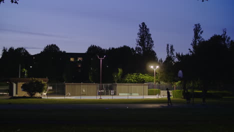 Silhouetted-people-play-one-on-one-basketball-on-outdoor-court-at-night