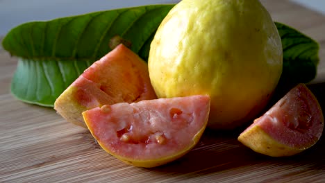 Zoom-in-on-whole-and-sliced-fresh-ripe-guava-fruit-with-leaves-on-cutting-board