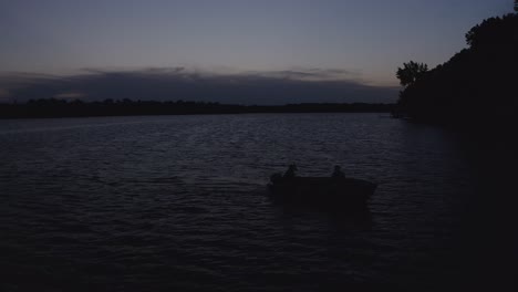 Aerial-shot-of-a-silhouetted-fishing-boat-on-lake-during-twilight