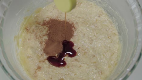 Pouring-teaspoon-of-vanilla-extract-into-yellow-batter,-Slowmo-Overhead-Closeup