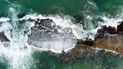 Beautiful-bird's-eye-top-aerial-drone-static-shot-of-waves-crushing-into-a-black-rock-in-the-beach-at-Sibauma-creating-a-natural-swimming-pool-during-low-tide-near-Pipa-in-Northern-Brazil