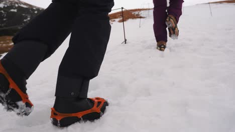A-couple-walking-an-uphill-trail-in-icy-snow-with-crampons-on-their-shoes