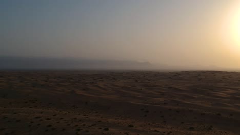 Drone-flying-through-the-desert-during-sunset-while-sand-dunes-are-moving-towards-the-viewer-whith-mountains-in-the-background-at-Wahiba-Sands-in-Oman