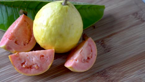 Ganze-Und-In-Scheiben-Geschnittene-Frische-Gelbe-Und-Rosafarbene-Guave-Frucht-Auf-Holzhintergrund,-Nahaufnahme