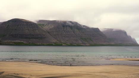 Stable-shot-of-girl-standing-on-white-sand-beach,-foggy-mountainscape