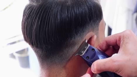 Hairdresser-with-a-hair-clipper-cuts-a-man-in-a-chair-in-a-barbershop-salon-using-an-electric-hair-clipper