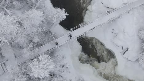 2-Personas-Caminando-En-La-Nieve-Sobre-Un-Puente-Con-Cascadas-Debajo