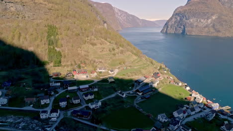 Aerial-drone-backward-moving-shot-of-village-houses-along-mountain-slope-with-river-passing-by-in-Norway-during-a-sunny-morning