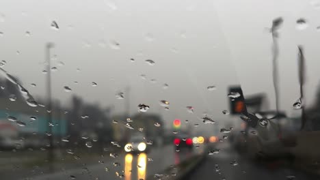 Schlechtes-Regenwetter-Mit-Regentropfen,-Die-Auf-Der-Windschutzscheibe-Herunterrutschen,-Und-Verschwommenen-Lichtern-Des-Autoverkehrs-Im-Hintergrund
