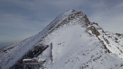 Lift-station-on-top-of-snowy-mountain-during-sunny-day-in-Austria---Aerial-view