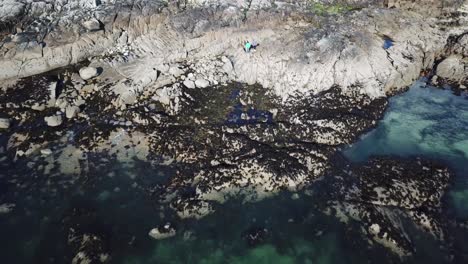 Luftaufnahme-Eines-Strandes-Aus-Felsen-In-Connemara,-Menschen-Stehen-Auf-Einer-Klippe