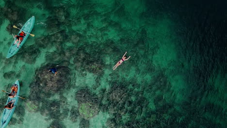 Aerial-shot-of-a-girl-floating-on-seawater-with-people-kayaking-around