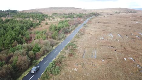 aerial-view,-Irish-landscape-in-Connemara:-road-with-a-driving-car,-fir-forest