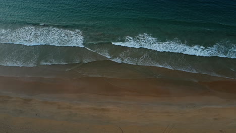 Aerial-drone-shot-of-ocean-waves-crashing-on-sandy-beach
