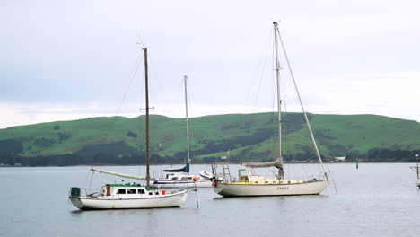 Drei-Segelboote-Vor-Anker-An-Einem-Düsteren,-Bewölkten-Tag,-Inselhügel-Im-Hintergrund