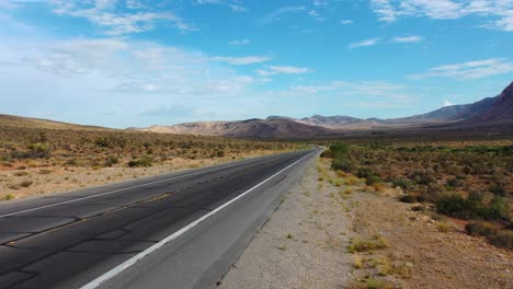 Cinematic-shot-of-an-empty-road-highway-with-mountains-at-Red-Rock-Canyon-in-Nevada’s-Mojave-Desert,-USA