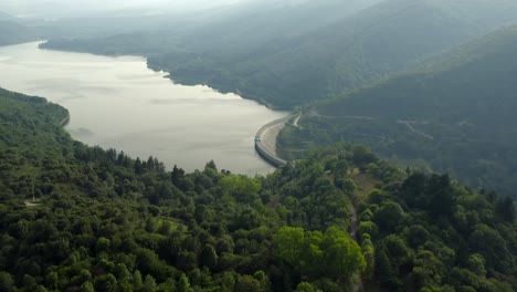 Drone-flyover-Beautiful-Ordunte-Lake,-Reservoir-dam-surrounded-by-Forested-hills,-Spain