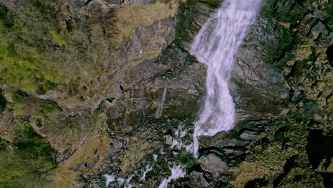 Top-down-shot-over-waterfalls-along-rocky-mountain-cliff-at-daytime