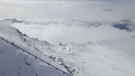Luftaufnahme-Der-Gondel,-Die-Schneebedeckte-Berge-österreichs-Bergab-Fährt---Dichte-Wolken,-Die-Das-Tal-Bedecken