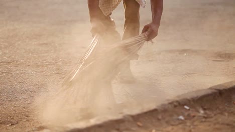 Man-is-sweeping-the-streets-in-a-dry-climate,-cleaning-dust-and-dirt-from-the-street-edge