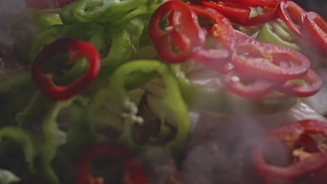 Adding-onions,-peppers-and-zucchini-slices-to-cooked-spicy-meat-for-mexican-food,-very-close-up-view