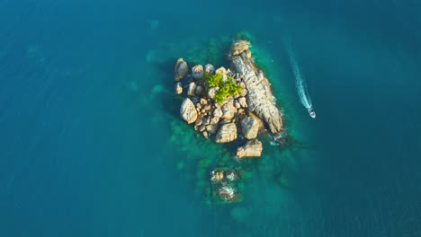 Drone-bird-eye-shot-over-island-and-passing-boat,-l'ilot-a-small-island-near-Mahe-on-the-north-coast,-great-place-for-doing-snorkelling-and-diving