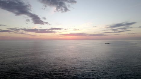 Aerial-dolly-forward-of-a-vibrant-sun-setting-on-the-horizon-over-the-ocean