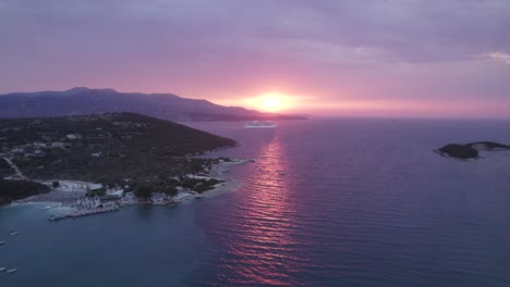 Vibrant-sunset-with-cruise-ship-passing-by-in-Mediterranean,-aerial-along-Ionian-coastline-of-Ksamil,-Albania