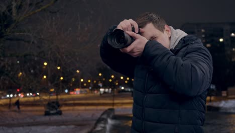 Young-male-tourist-takes-photos-at-night-in-city,-takes-a-look-on-picture-and-smiles
