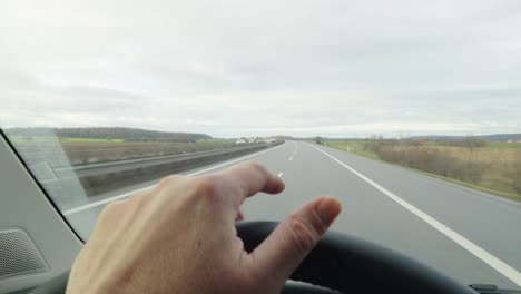POV-of-a-hand-on-the-steering-wheel-tapping-to-the-beat-while-driving-on-the-highway