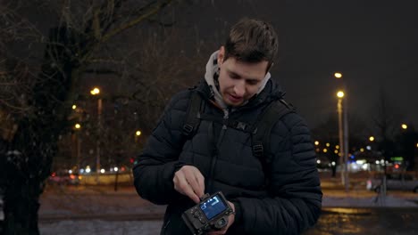 Young-backpacker-photographer-adjusting-digital-camera-gear-at-night-in-city-outdoors