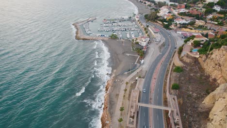 Aerial-birds-eye-shot-of-cars-on-road-beside-ocean-with-marina-of-Malaga-in-background---Static-top-down