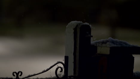 Wooden-Post-Beside-Iron-Gate-Covered-In-Snow-At-Night