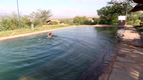 Tracking-shot-of-a-man-swimming-alone-in-a-pool-in-Rift-Valley,-Tanzania