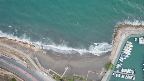 Aerial-top-down-shot-of-marina-with-Yachts-and-crashing-waves-reaching-candado-beach-in-Malaga