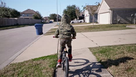 Un-Niño-Monta-Su-Bicicleta-En-Una-Acera-A-Través-De-Su-Vecindario-A-Baja-Velocidad-De-4k