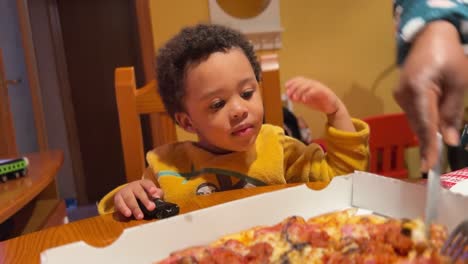 Entzückendes-Und-Sehr-Ausdrucksstarkes-Zweijähriges-Schwarzes-Baby,-Das-Ungeduldig-Darauf-Wartet,-Die-Pizza-Zu-Essen,-Die-Seine-Mutter-Zu-Hause-Schneidet