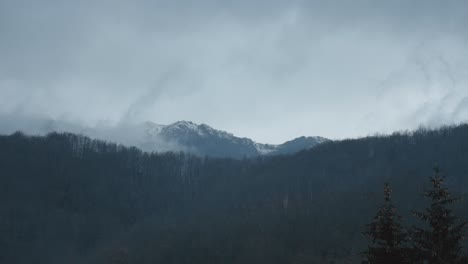 Clouds-time-lapse-over-mountain,-trees-and-fog