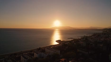 Luftaufnahme-Der-Küstenlinie-In-Malaga-Mit-Wunderschönem-Goldenem-Sonnenuntergangslicht,-Das-Sich-Hinter-Der-Bergkette-Versteckt