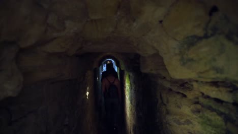 Tourists-Walking-Exploring-Deep-Long-Underground-Rocky-Tunnel,-roman-sewers-in-Medina,-Cadiz,-Spain