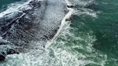 Beautiful-bird's-eye-top-aerial-drone-shot-of-waves-crushing-into-a-black-rock-in-the-beach-at-Sibauma-creating-a-natural-swimming-pool-during-low-tide-near-Pipa-in-Northern-Brazil