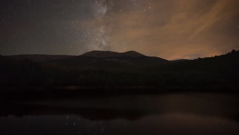 Night-time-lapse-of-the-movement-of-the-stars-and-the-Milky-Way-over-the-Moncayo-mountain,-with-reflection-in-the-lake