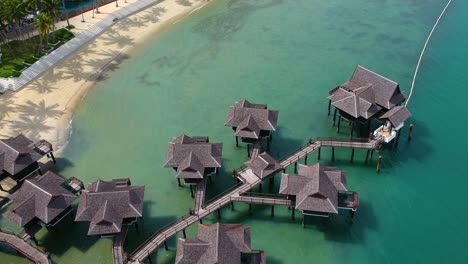 Aufsteigende-Und-Aufbauende-Luftaufnahme-Von-Pfahlbauten-Und-Wunderschönem-Strand-Mit-Türkisfarbenem-Wasser-In-Einem-Resort-Auf-Der-Insel-Pangkor-Im-Westen-Malaysias
