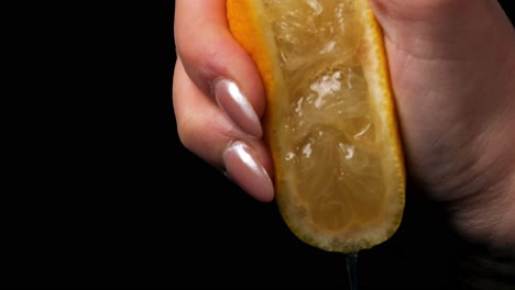 Static-slow-motion-shot-of-yellow-ripe-lemon-squeeze-with-leaking-juice-held-by-a-beautiful-manicured-woman's-hand-against-a-black-background
