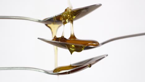 Mesmerizing-view-of-golden-honey-dripping-down-through-three-spoons-on-white-background