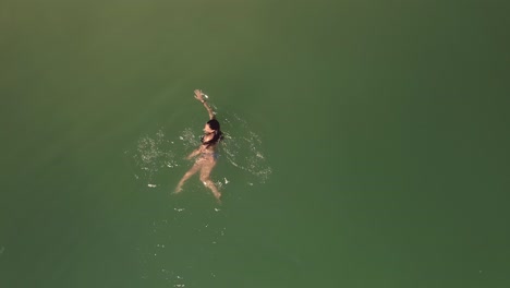 Aerial-directly-above-female-in-bikini-swimming-in-beautiful-green-ocean-surface